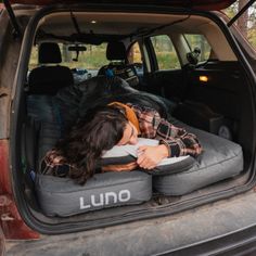 a woman sleeping in the back of a truck with her head down on an air mattress