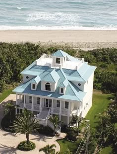 an aerial view of a large white house on the beach with blue roof and shuttered windows