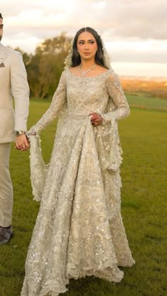 a man and woman dressed in wedding attire holding hands while standing on green grass with trees in the background