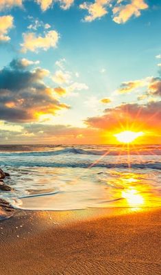 the sun is setting over the ocean with waves coming in to shore and rocks sticking out of the sand