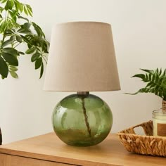 a green glass lamp sitting on top of a wooden table next to a potted plant