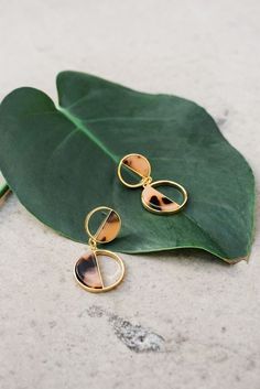 a pair of gold earrings sitting on top of a green leaf next to a plant