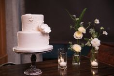 a white wedding cake sitting on top of a table next to two vases filled with flowers