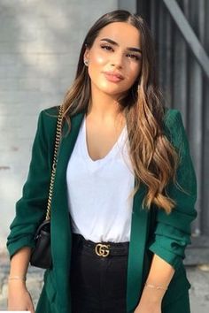 a woman with long hair wearing a green blazer and black pants, standing on the street