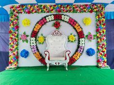 a white chair sitting in front of a flower covered stage with flowers on the wall