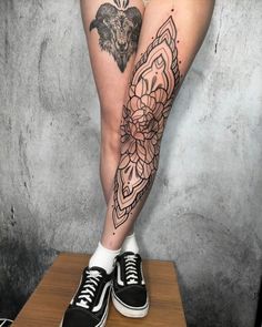 a woman's legs with tattoos and flowers on her leg, standing on a wooden platform