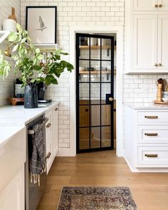 a kitchen with white cabinets and wood floors, an area rug and a black door