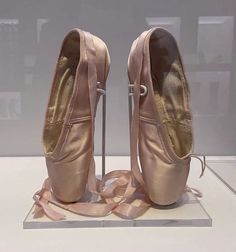 a pair of ballet shoes on display in a glass case with ribbon around the ankles