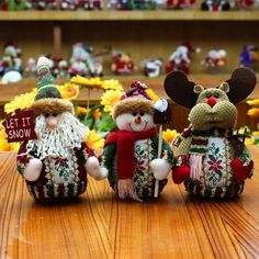 three knitted snowmen sitting next to each other on top of a wooden table