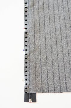 a piece of gray fabric with black pins on it and some white thread next to it