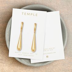 two gold earrings sitting on top of a white card