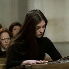 a woman sitting at a desk with an open book in front of her and other people behind her