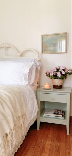 a white bed sitting next to a small table with flowers on it and a candle