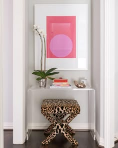 an animal print stool sits in front of a white table with a pink painting on it