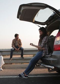 two people are sitting on the back of a car and one is holding a cell phone