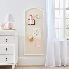 there is a white cabinet with pictures on it and a lamp next to the window