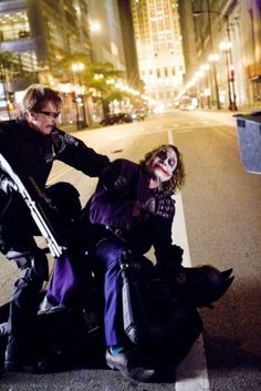 two people dressed up as the joker and harley on a city street with buildings in the background