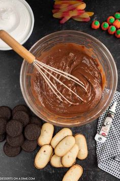 a bowl filled with chocolate frosting next to cookies