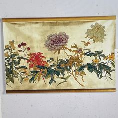 a painting hanging on the wall with flowers and leaves painted on it's side