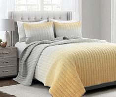 a bed with yellow and grey comforters in a bedroom next to a white rug