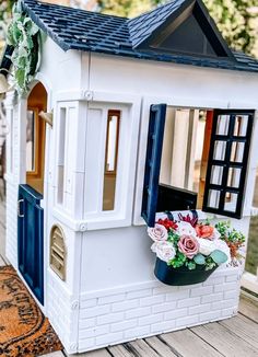 there is a doll house that has flowers in the window and on the front porch