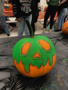 a pumpkin with green and orange paint on it's face sitting on a table