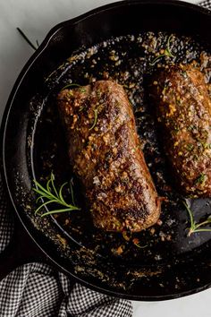 two steaks cooking in a skillet with herbs and seasoning on the side