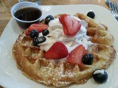 a waffle with strawberries and blueberries on top sits on a white plate