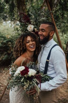 a man and woman standing next to each other in front of trees with flowers on them