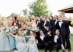 a large group of people in formal wear posing for a photo with their hands up