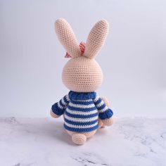 a crocheted stuffed rabbit wearing a blue and white striped shirt sits on a marble surface