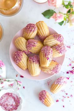 pink sprinkled donuts are on a plate next to glasses and napkins