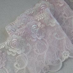 two pieces of white lace with pink flowers on top of each other, sitting on a table