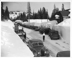 an old black and white photo of cars parked on the side of a snow covered road