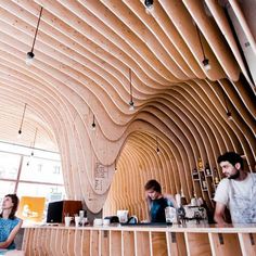 people are sitting at the bar in an unusual restaurant with wood slats on the ceiling