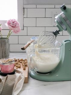 a mixer with some food in it on a counter next to flowers and other items