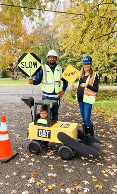 a man and woman standing next to a child in a construction vehicle with a sign that says slow