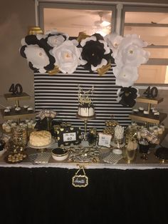 a table topped with lots of cakes and desserts covered in black and white paper flowers