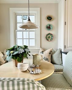 a dining room table and chairs with plates on the wall next to it, in front of a window