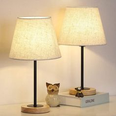 two lamps sitting on top of a table next to a book and cat figurine