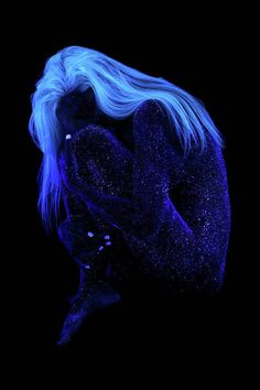 a woman with blue hair is sitting in the dark and has her hands on her face