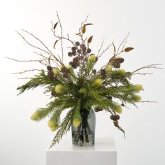 a vase filled with green and yellow flowers on top of a white table next to a wall