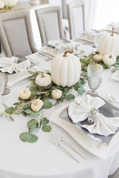 the table is set with white pumpkins, greenery and napkins on it