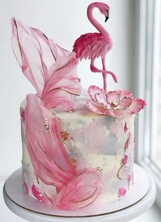 a pink flamingo cake sitting on top of a white table next to a window