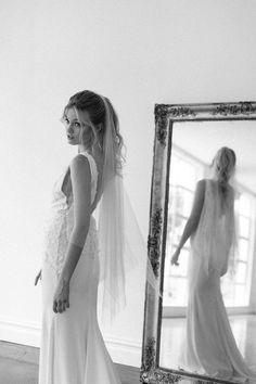 a woman standing in front of a mirror wearing a wedding dress with a veil on her head