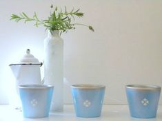 four blue glass cups sitting next to a white vase with a plant in the middle