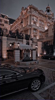 a black car parked in front of a large building at night with street lights on