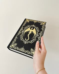 a hand holding a black and gold book with a golden dragon on it's cover