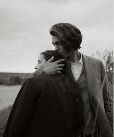 black and white photograph of two people standing next to each other in front of a body of water