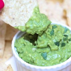 guacamole being dipped into a small white bowl with tortilla chips